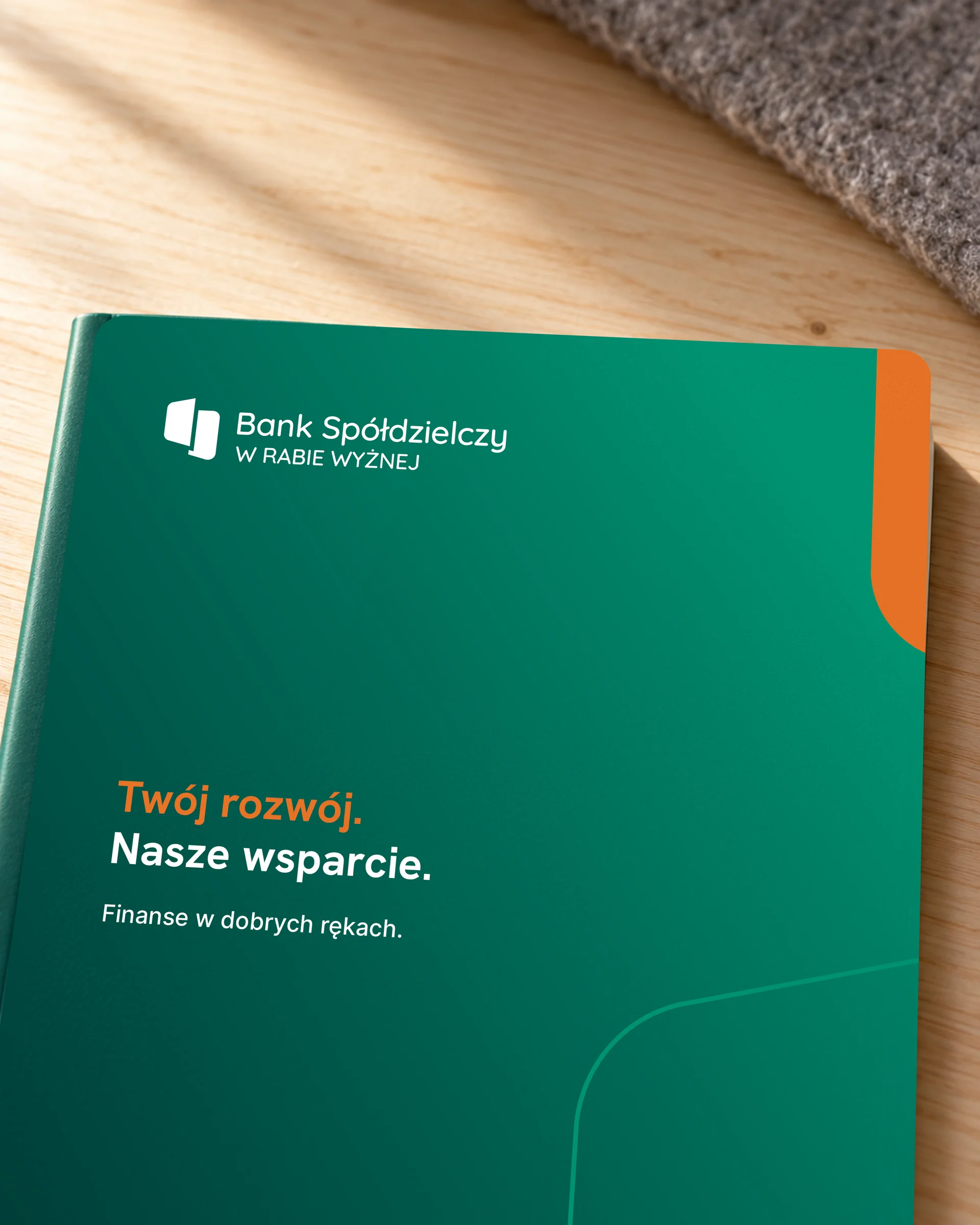Okładka notesu banku z hasłem „Twój rozwój. Nasze wsparcie.” w bocznym świetle