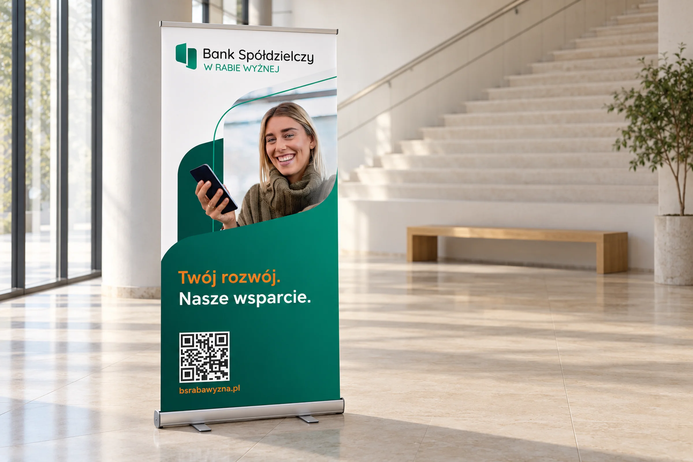 Roll-up banku z kobietą przy telefonie i hasłem marki w jasnym holu