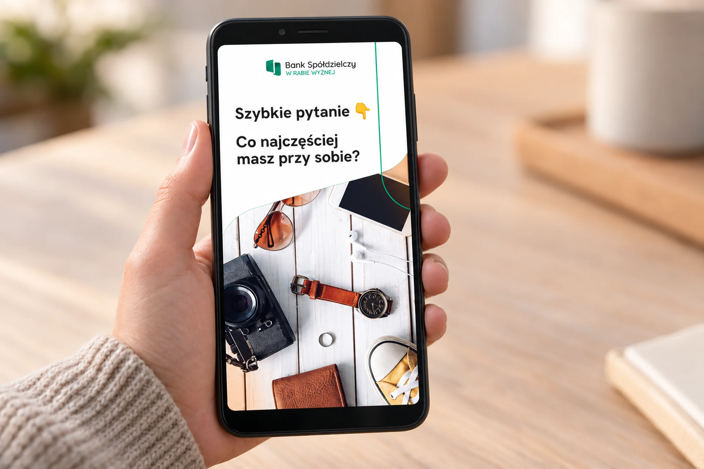 Dłoń trzyma telefon ze story banku „Szybkie pytanie: co najczęściej masz przy sobie?”